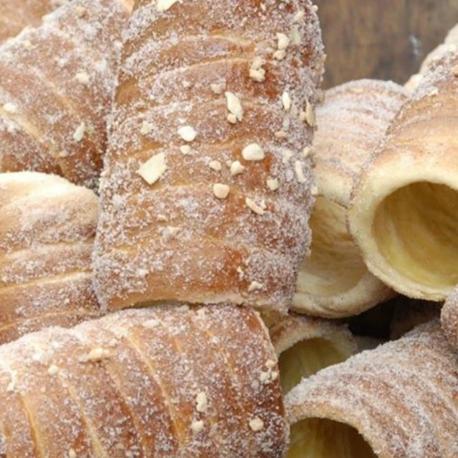 Trdelníky posypané cukrem a ořechy po pečení.