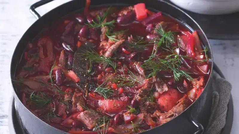 Hot borscht with beef, beans and herbs in iron pot.