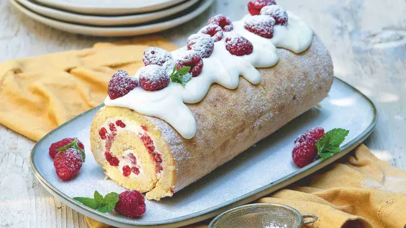 Překrásná roláda z piškotu s mascarpone, malinami a cukrem na talíři.