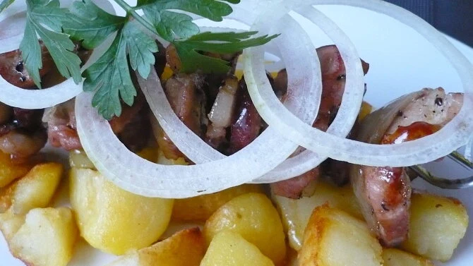Pecené špízy s bramborami a cibulovými kroužky na talíři.