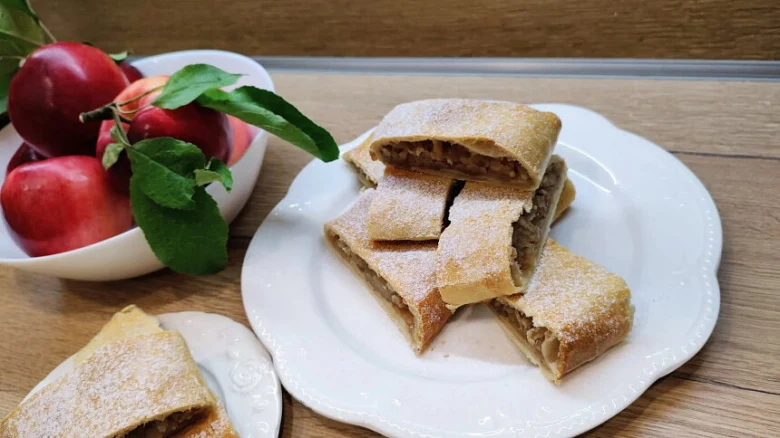 Kusky jablkového štrúdlu s moučkovým cukrem vedle misky jablek.