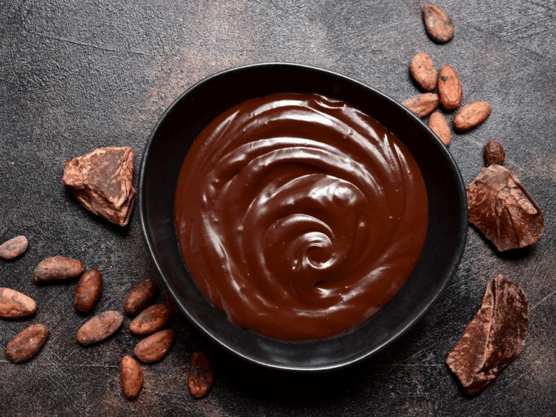 Čokoládová ganache v černé misce s kakaovými bobulemi.