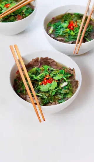 Tři misky vietnamské polévky pho s bylinkami a čili.