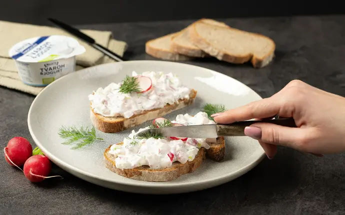 Rozmazaná pomazánka z tvarohu s ředkvičkami na chlebovém plátku.