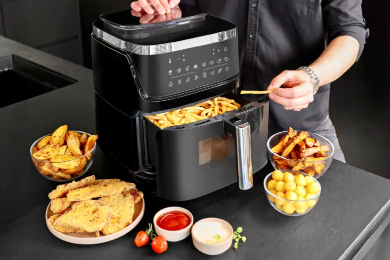 Člověk připravuje hranolky v horkovzdušné fritéze s dalšími smaženými jídly.