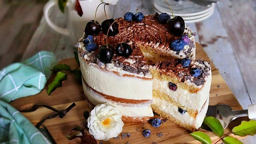 Nepečený dort s mascarpone, šlehačkou a ovocem na dřevěném podnosu.
