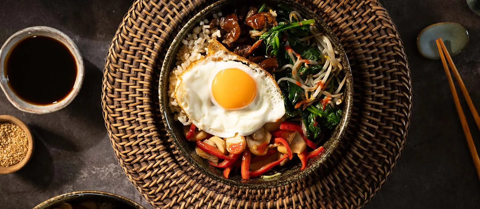 Bibimbap s vejcem a zeleninou v keramické mísce.