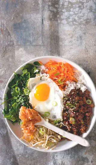 Bibimbap s vejcem a zeleninou v bílé misce.