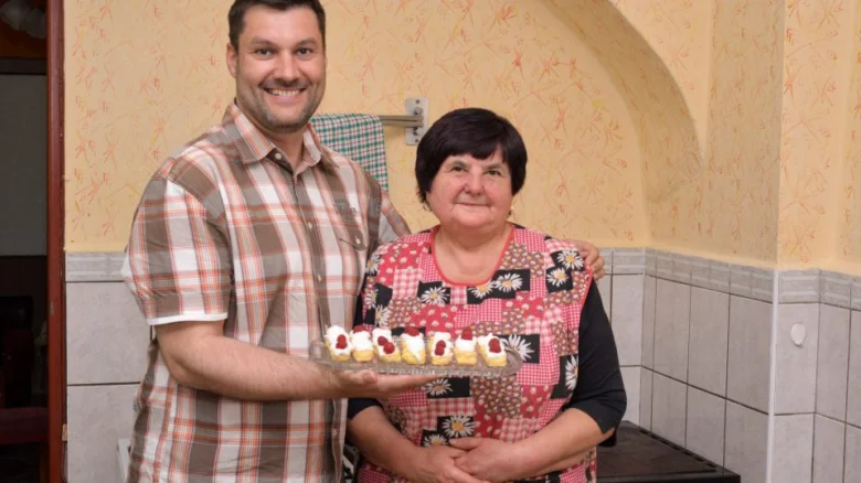 Muž drží talíř s rakvičkami vedle starší ženy v kuchyni.