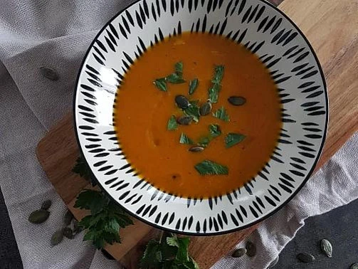 Miska s dýňovou polévkou ozdobená bylinkami.
