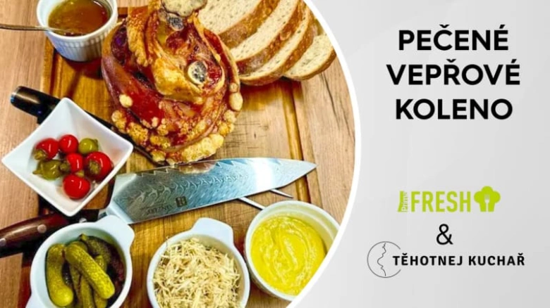 Pečené vepřové koleno s chlebem a přílohami na dřevěném talíři.