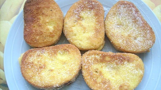 Zlatavé vaječné smažky posypané cukrem na talíři.