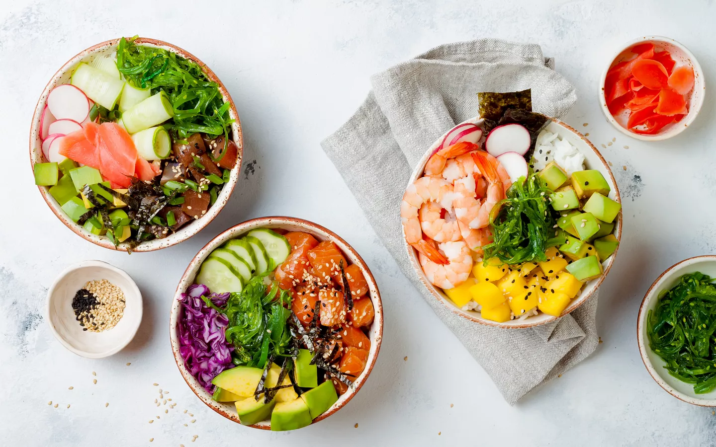 Tři barevné poke bowl s čerstvými ingrediencemi jako losos, avokádo a mořské řasy.