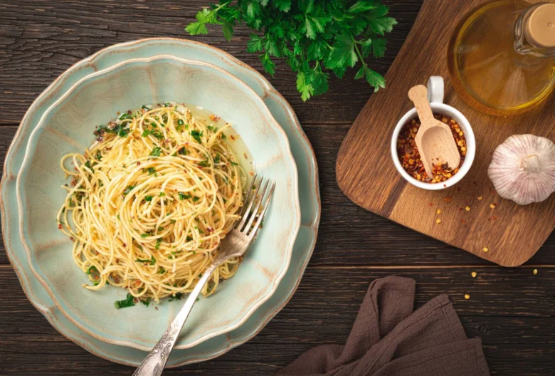 Pasta s česnekem, olejem a petrželkou na dřevěném stole.