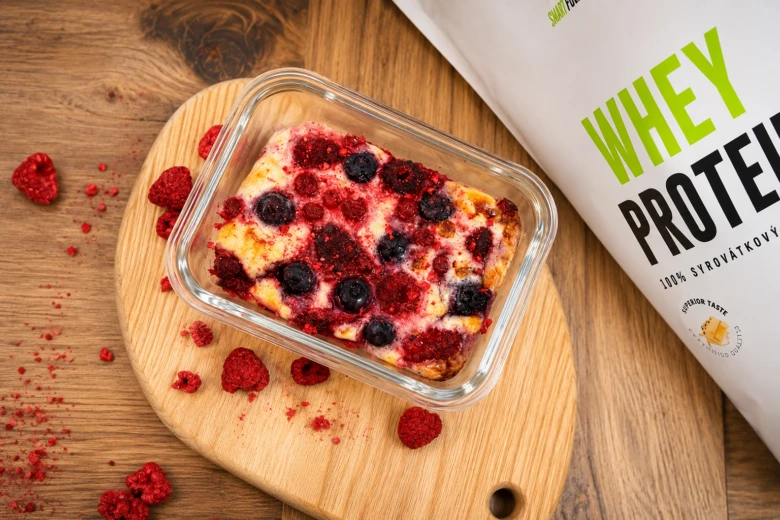Pečený tvaroh s ovocem v skleněné nádobce vedle prášku Whey Protein.