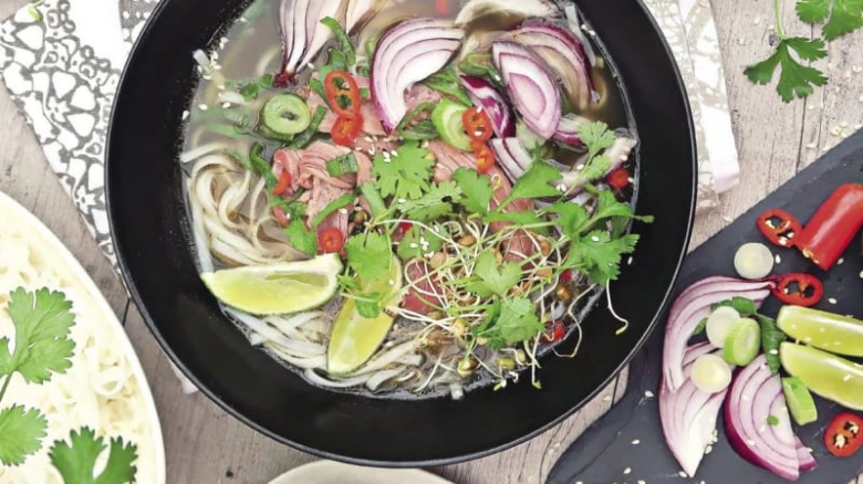 Černá miska s vietnamskou polévkou Pho se zeleninou a bylinkami.
