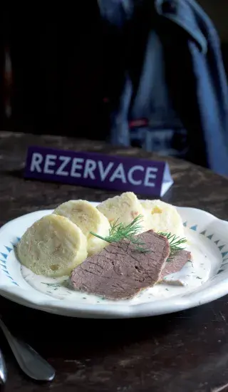 Párek hovězího masa s koprovou omáčkou a knedlíky na talíři.
