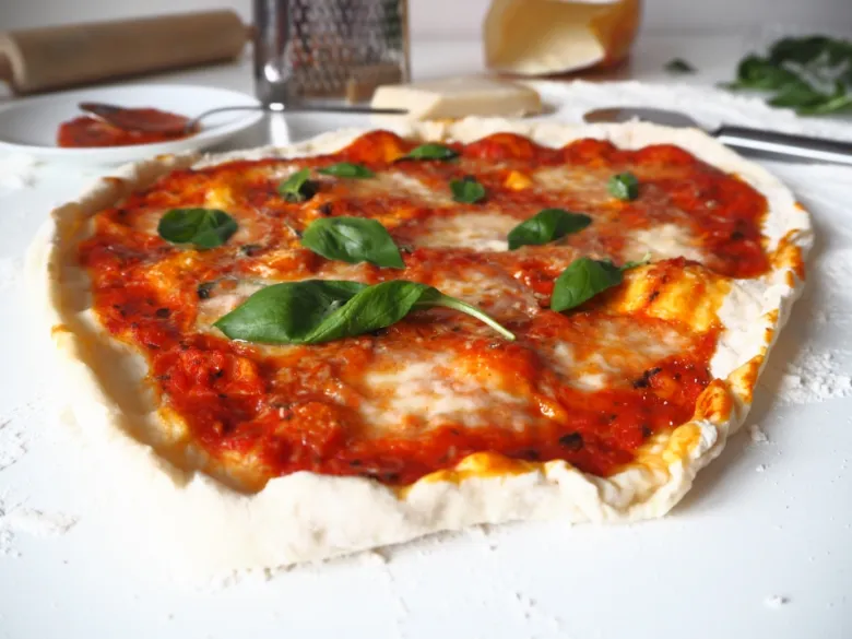 Čerstvě upečená italská pizza s bazalkou na bílém povrchu.