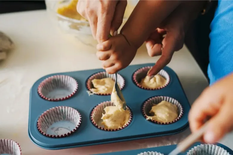 Dospělí a dítě nalévají těsto do formiček na muffiny.