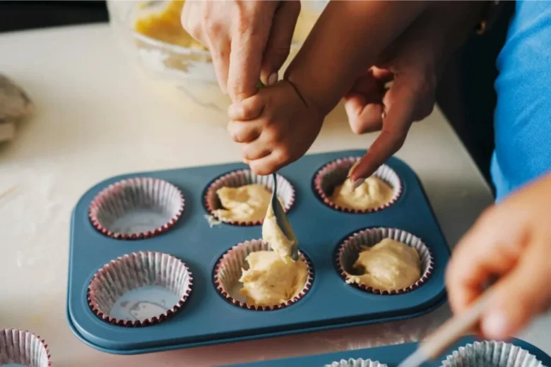 Ruce nalévají těsto do formiček na muffiny.