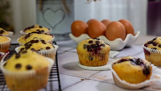 Svěží bezlepkové muffiny s borůvkami vedle vajec na přípravu.