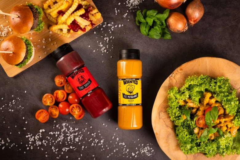 Dvě lahve omáčky s chilli mezi čerstvými ingrediencemi jako rajčata, bazalka a salát.