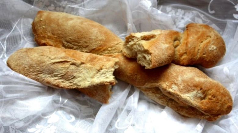Zlatohnědé domácí bagety a francouzské pečivo na bílém krajkovém ubrusu.