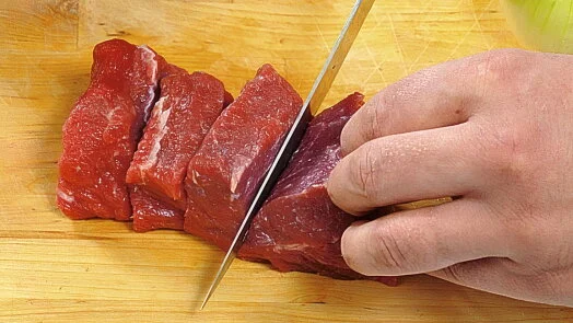 Rozkrojování syrového hovězího masa na proužky nožem.