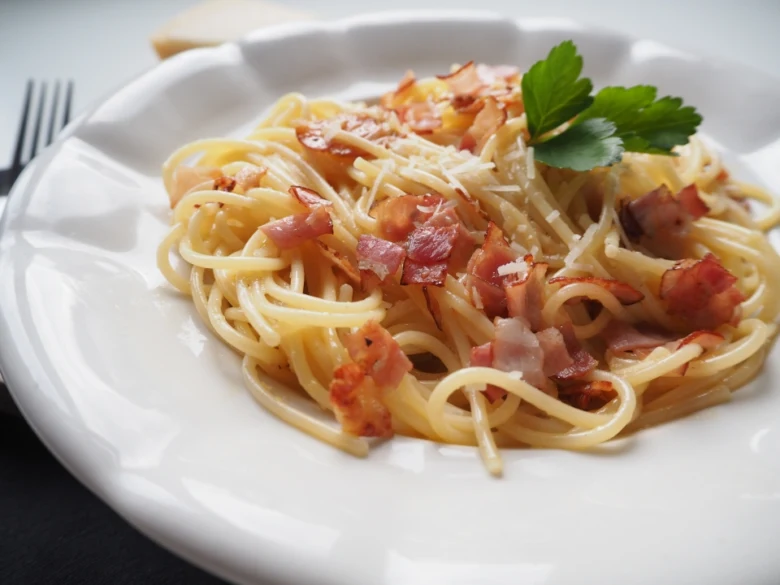 Spaghetti Carbonara s podaný na bílém talíři se šunkou.