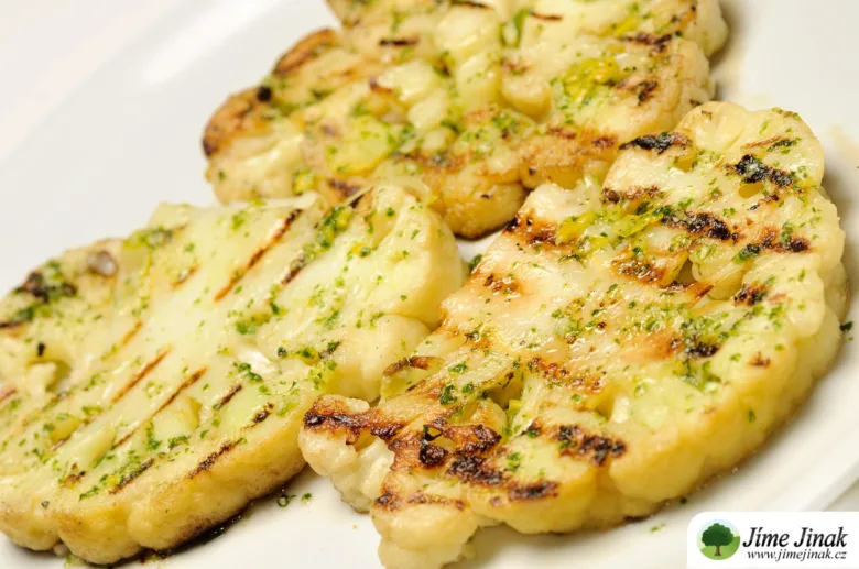 Grilované květákové steak s bylinkami na bílém talíři.