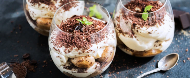 Tři skleničky s dezertem tiramisu posypané kakaem.