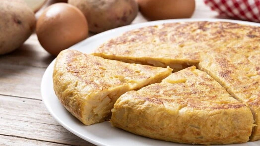 Hotová vaječná smaženka s bramborami na bílém talíři.