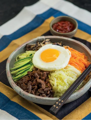Korejský bibimbap s vejcem, masem a zeleninou v kamenné misce.