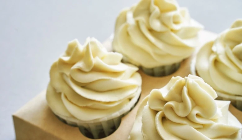 Čtyři muffiny s krémovou máslou na dortu v dřevěném držáku.