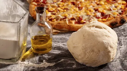 Kulka těsta na pizzu s olejem moukou a hotovou pizzou.