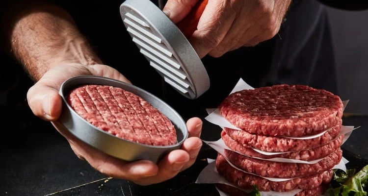 Muž tvaruje hovězí burgery v kovovém formě.