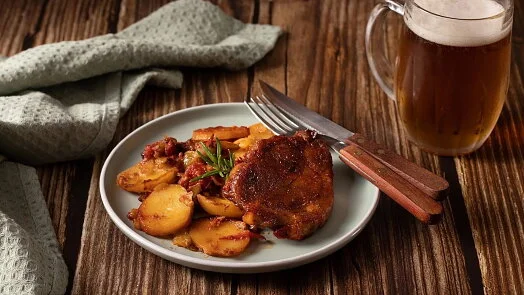Pečená vepřová krkovice s bramborami a pivem na talíři.