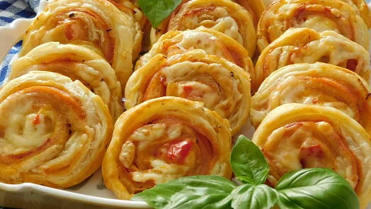 Mini pizzy z listového těsta s rajčaty a sýrem na bílém talíři.