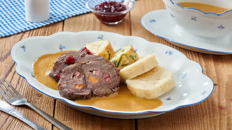 Příprava tradičního jídla: plátek masového koláče s knedlíkem.
