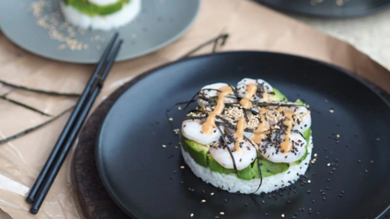 Sushi s rýží, avokádem a krevetkami na černém talíři.