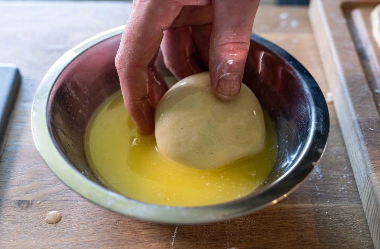 Ruka mává kynuté těsto do mísy s rozpuštěným máslem.