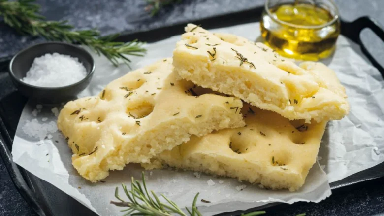 Zlatá focaccia s bylinkami a olivovým olejem na papíře.