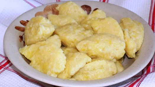 Připravené žluté halušky s brynzou v misce na ubrousku.