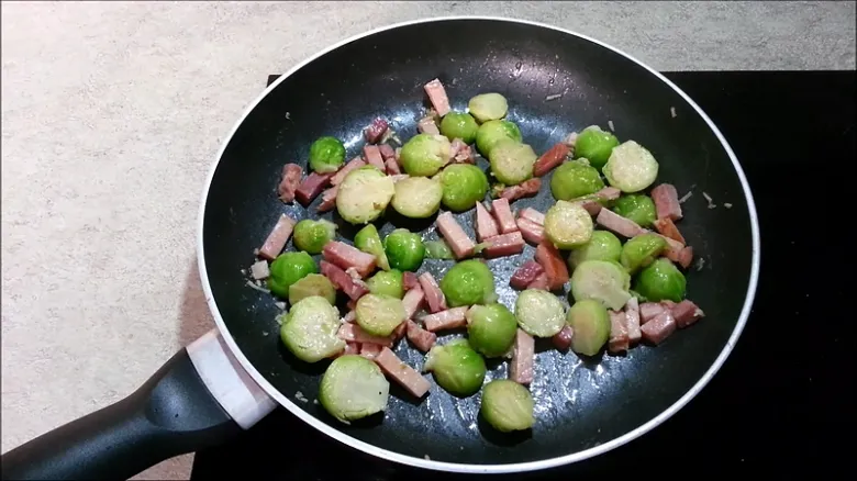 Růžičková kapusta smažená se slaninou a masem na pánvi.