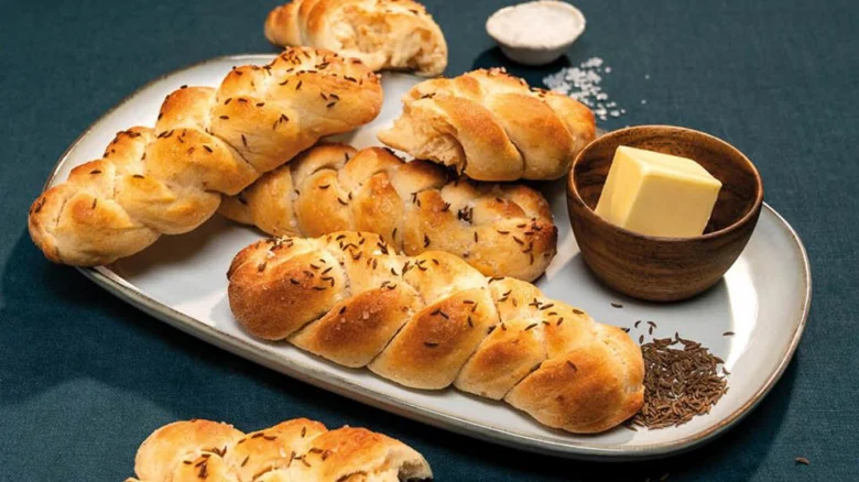 Zlaté loupáky s semínkem podávány s máslem na tmavě modrém pozadí.