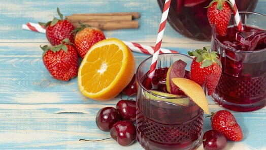 Sklenice s červenou sangrií ozdobená jahodami, pomerančem a hruškou.