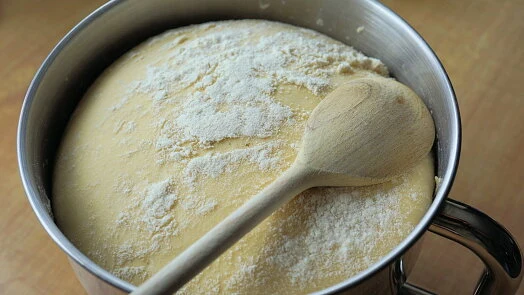 Kyslá těsto v míse posypané moukou s dřevěnou lžící.