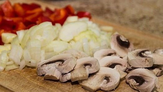 Naškrábané zeleniny: papriky, cibule a houby na prkénku.