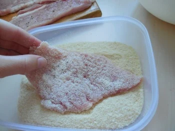 Ruka položí kus masa do mletých sušenek pro obalení.