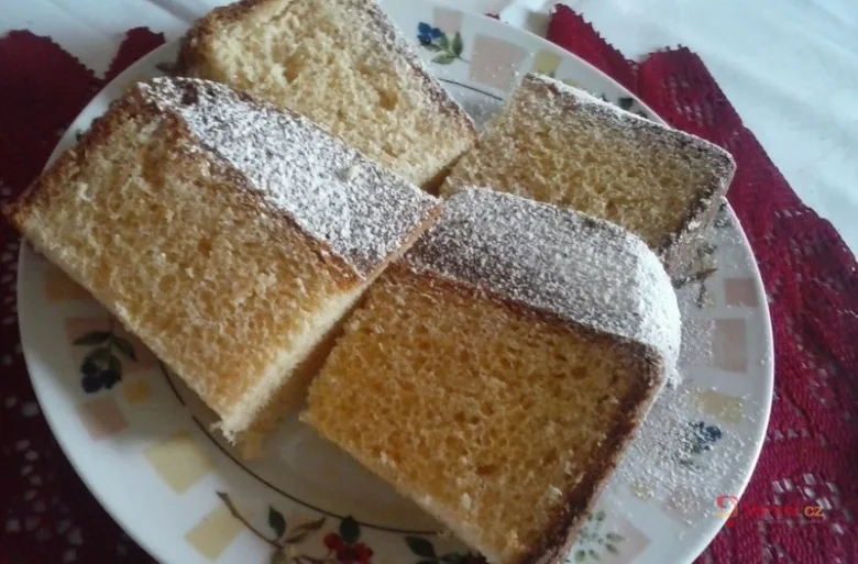 Čtyři kousky kynutého koláče posypané moučkovým cukrem na talíři.